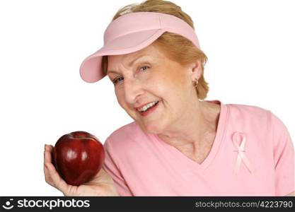 ...keeps the doctor away. A senior woman dressed for breast cancer awareness holding a bright red apple. Isolated on white.
