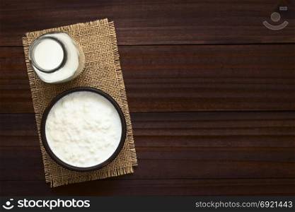 Kefir grains in milk in bowl with bottle of milk on the side, photographed overhead with natural light. Kefir