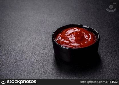 Ketchup in a ceramic saucepan. Black concrete background. Red tomato sauce ketchup in a black ceramic saucepan