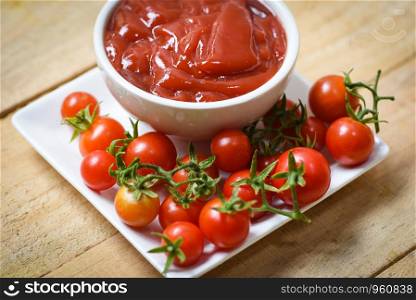 Ketchup in cup and fresh tomatoes on white plate / Close up tomato sauce on wooden background
