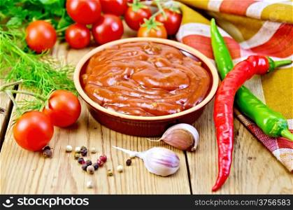 Ketchup in pottery, tomatoes, parsley, hot pepper, garlic, napkin, on a background of wooden boards
