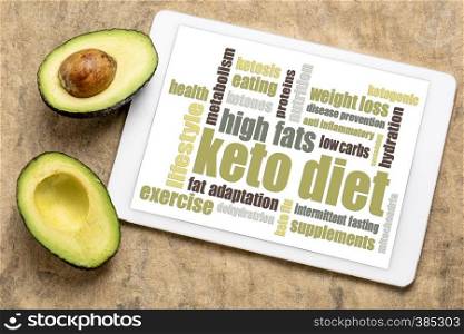 keto diet word cloud on digital tablet with a cut avocado against bark paper