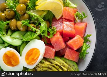 Ketogenic, paleo diet lunch bowl with salted salmon fish, lemon, avocado, olives, boiled egg, cucumber, green lettuce salad and chia seeds, healthy food trend, top view
