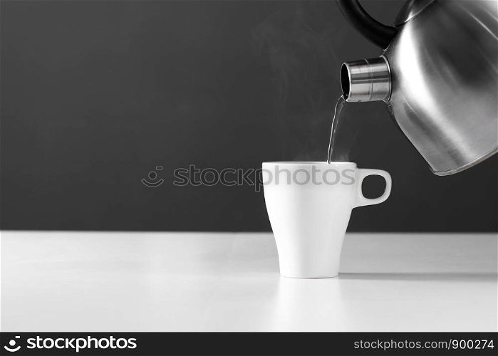 kettle pouring boiling water into a cup with smoke on wood table. retro kettle pouring water into a cup on a dark background with smoke on wood table