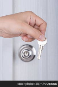 key in hand with door knob and white door background