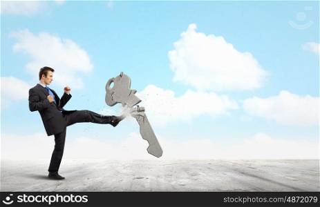 Key to success. Angry businessman crashing stone key with kick