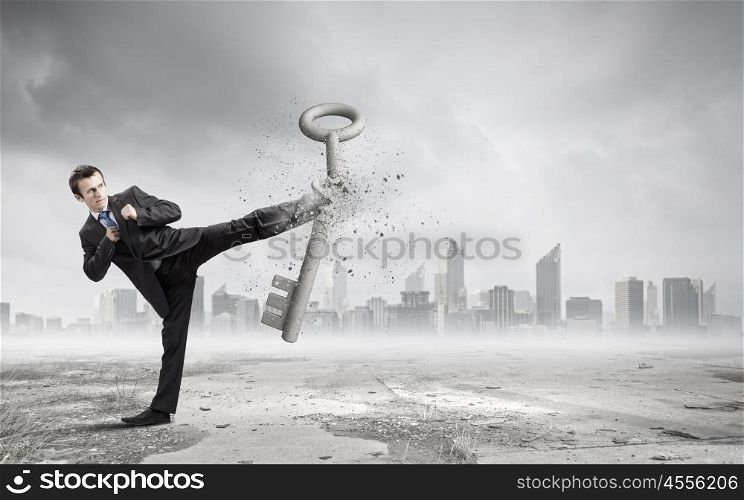 Key to success. Angry businessman crashing stone key with punch