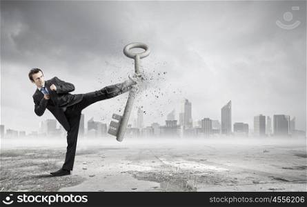 Key to success. Angry businessman crashing stone key with punch