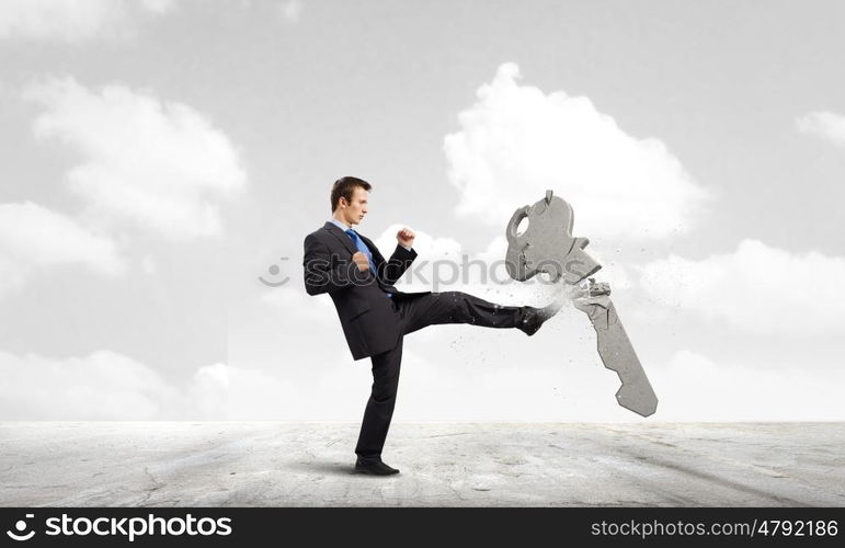 Key to success. Angry businessman crashing stone key with punch