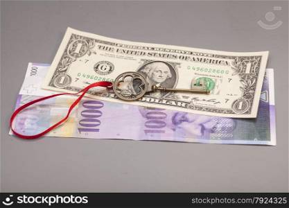 Key To Success With Red Bow on One American dollars and 1000 Swiss franc currency on gray