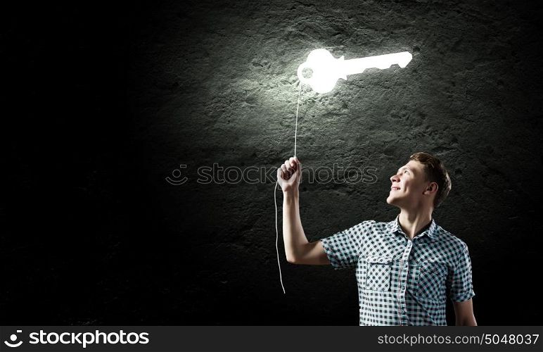 Key to success. Young man catching key against dark background