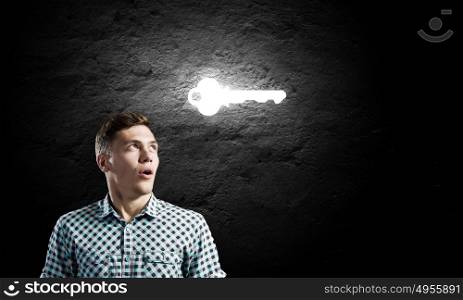 Key to success. Young man with key against dark background