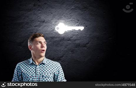 Key to success. Young man with key against dark background