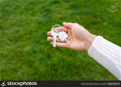 Keys with a keychain in the form of a metal house from a new house or apartment in the hands of a girl against a background of green grass. Keys with a keychain in the form of a metal house from a new house or apartment in the hands of a girl against a background of green grass.