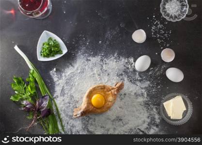 Khachapuri on black table with flour and ingridients. Top view. Khachapuri on black table with flour