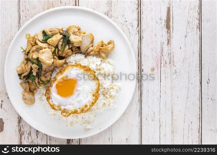 Khao Pad Ka Prao Gai Kai Dao, Thai food, streamed rice topped with basil stir fried chicken and fried egg in white ceramic plate on white old wood texture background with copy space for text, top view