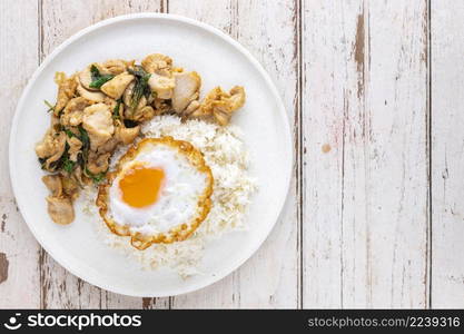 Khao Pad Ka Prao Gai Kai Dao, Thai food, streamed rice topped with basil stir fried chicken and fried egg in white ceramic plate on white old wood texture background with copy space for text, top view