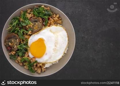 Khao Pad Ka Prao Kai Yeow Ma Kai Dao, Thai food, streamed rice with basil stir fried century egg, mince pork and fried egg in ceramic plate on dark grey texture background, top view
