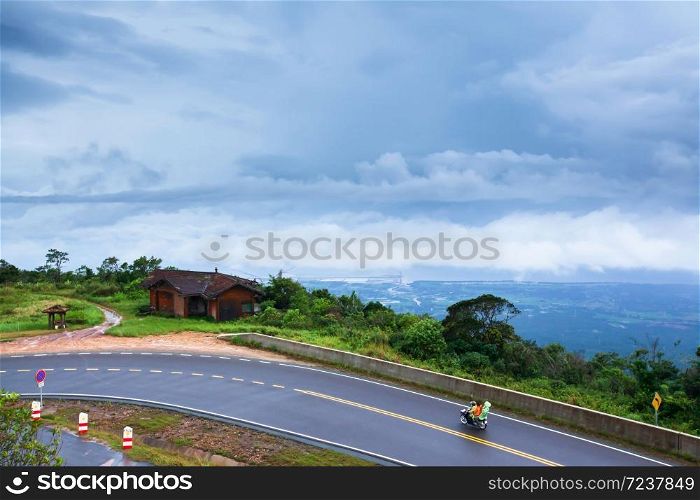 Khmer family driving motorcycle on the mountain asphalt road on a rainy day, cloudy covered the Gulf in the background. Kampot, South Cambodia.