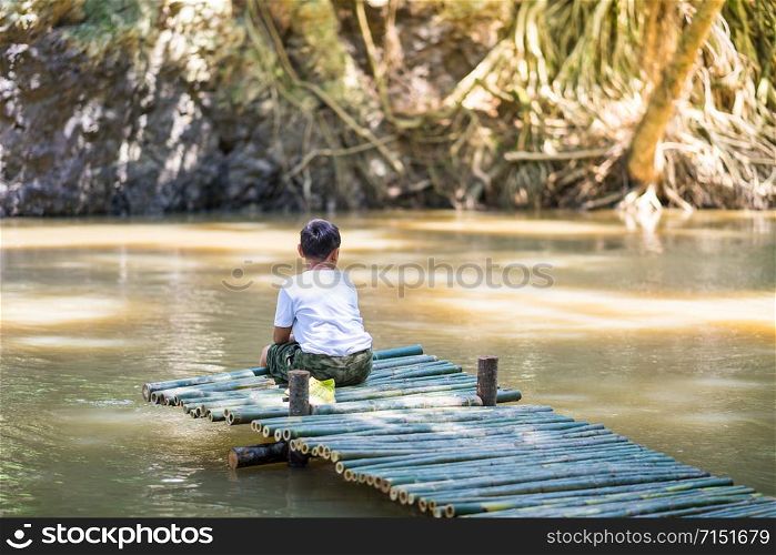 Kid boy sit on the Bamboo bridge beside the lake