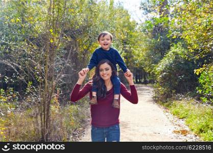 kid boy sitting on mother shoulders walking in the park trail