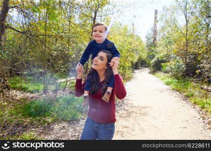 kid boy sitting on mother shoulders walking in the park trail