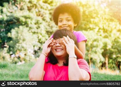 Kid covering mother's eyes in the green park with copy space - Daughter and mother relationship