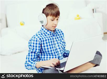 Kid enjoying leisure time. Boy of school age listening music from laptop through headphones while sitting on floor