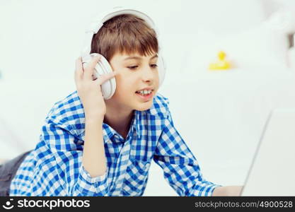 Kid enjoying leisure time. Boy of school age listening music from laptop through headphones while lying on floor