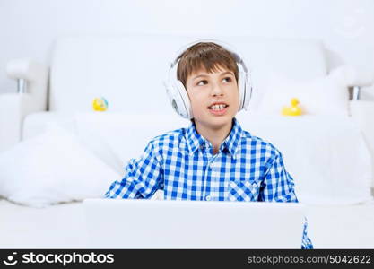 Kid enjoying leisure time. Boy of school age listening music from laptop through headphones while sitting on floor