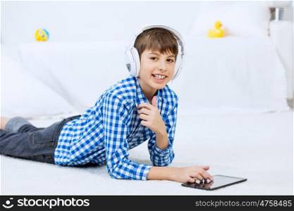 Kid enjoying leisure time. Boy of school age with headphones on head playing tablet game
