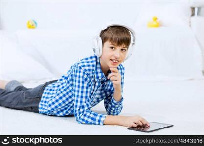 Kid enjoying leisure time. Boy of school age with headphones on head playing tablet game
