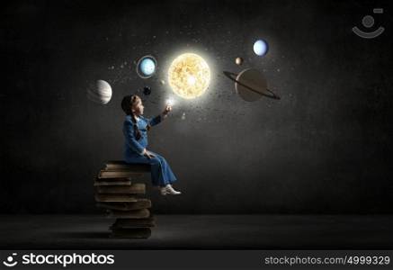 Kid girl explore space. Little girl sitting on stack of books and touching planet