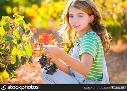 Kid girl happy smiling in autumn vineyard field holding grapes bunch on hand