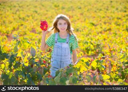 Kid girl in autumn vineyard field and holding red leaf in hand