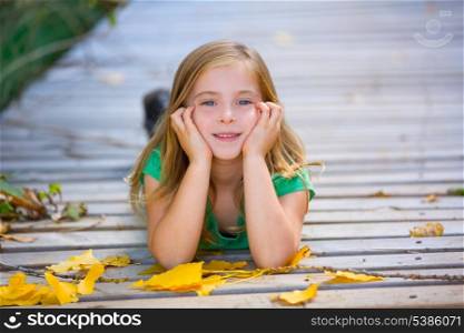 Kid girl in autumn wood deck with yellow leaves relaxed outdoor
