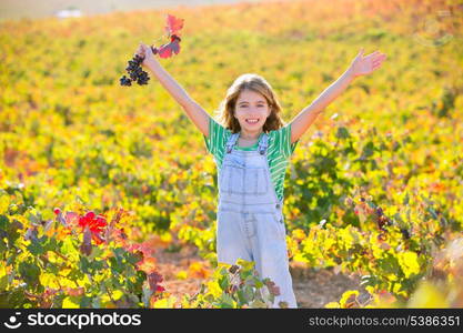 Kid girl in happy autumn vineyard field open arms with red leaf grapes bunch in hand