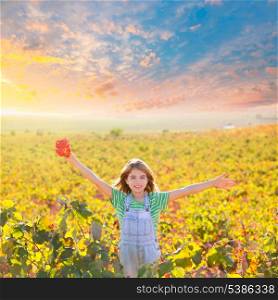 Kid girl in happy autumn vineyard field open arms with red leaf in hand