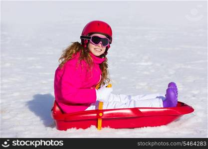 Kid girl playing sled in winter snow with helmet ang goggles