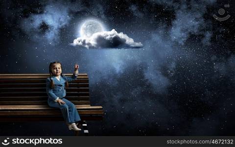 Kid girl pointing up. Little girl sitting on wooden bench and pointing with finger up