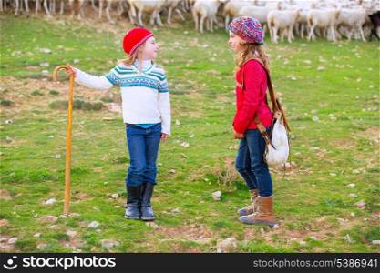 Kid girl shepherdess sisters happy with flock of sheep and wooden stick in Spain