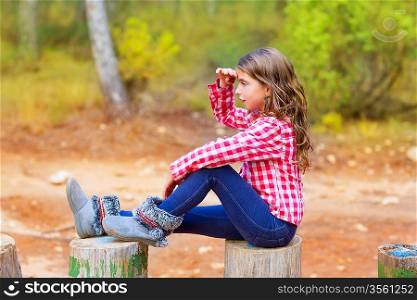 Kid girl sitting in forest trunk looking far away with hand in forehead