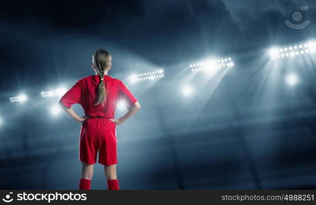 Kid girl soccer player. Full length photo of young girl standing in lights of stadium