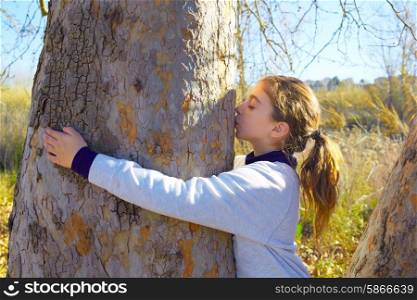 Kid girls loves nature hug annd kiss a tree tunk in outdoor winter park