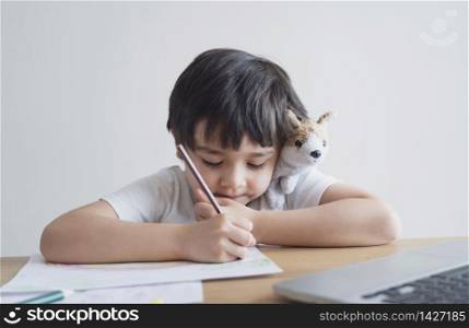 Kid in self isolation siting with notebook on table doing homework,Happy Child boy writing or drawing on white paper, Elementary school and home schooling, Distance Education,E-learning online concept