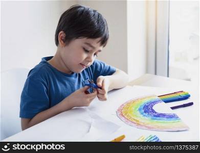Kid is isolation using scissors cutting paper in rainbow shape on white background, Children activities at home while school off.Stay at home Social media campaign for coronavirus prevention concept