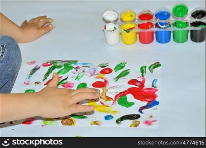 Kid paints with her fingers with different color paint