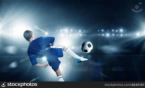 Kid play soccer on stadium. Rear view of kid boy in blue uniform on soccer stadium kicking ball