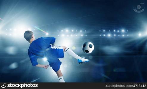 Kid play soccer on stadium. Rear view of kid boy in blue uniform on soccer stadium kicking ball