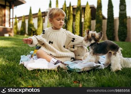 Kid play with funny dog in the garden. Child with puppy sitting on the lawn on backyard. Little girl and her pet having fun on playground outdoors, happy childhood. Kid play with funny dog in the garden